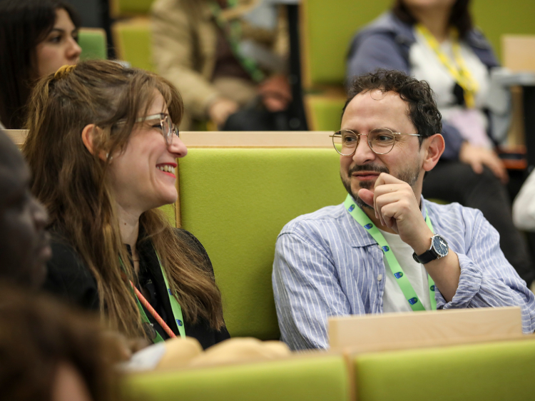 Two smiling people engaging in conversation in a lecture theatre.